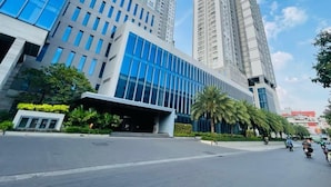 A modern building with multiple high-rise structures, a covered entrance, and palm trees lining the street.