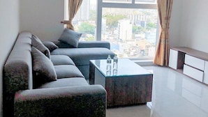 A modern living room with a sectional sofa, a glass coffee table, and a view of a cityscape through large windows.
