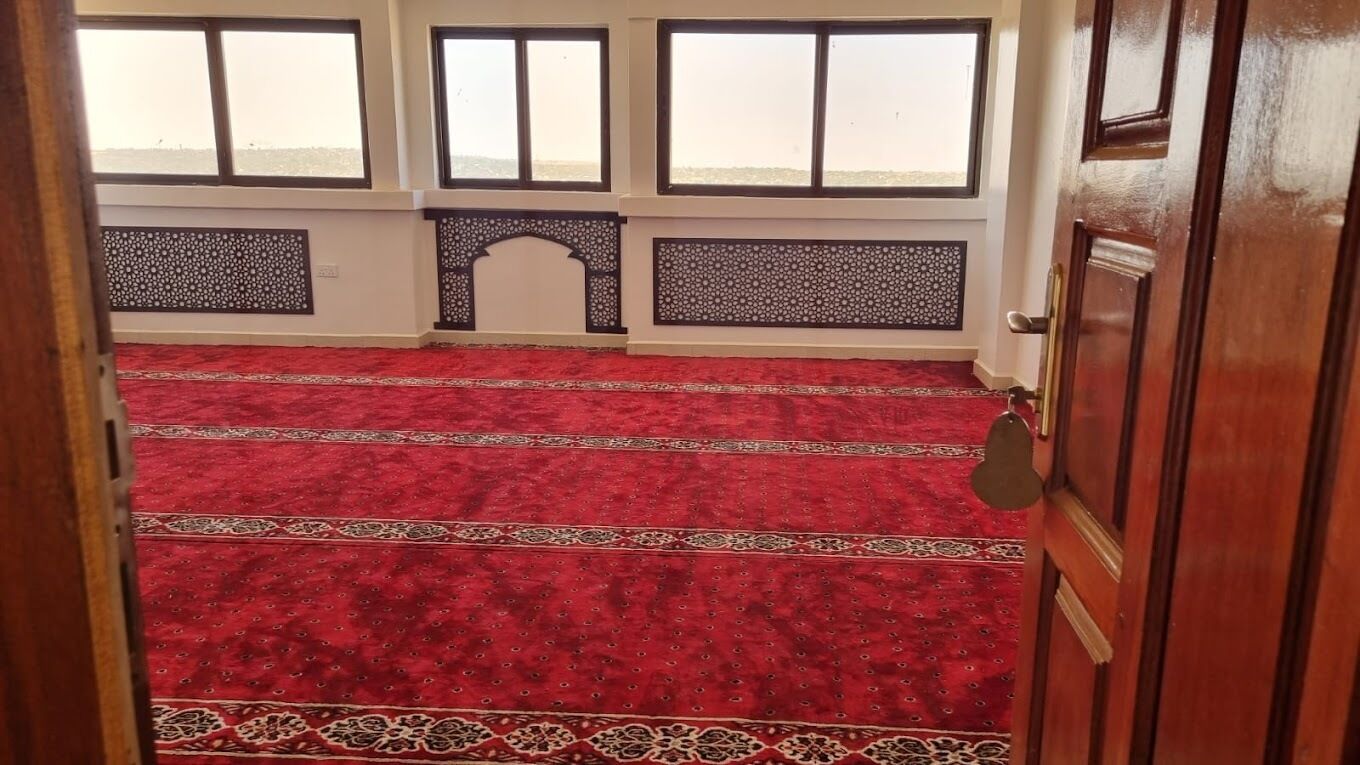 A room with a red carpet, wooden door, and windows with decorative grills.