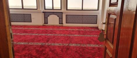 A room with a red carpet, wooden door, and windows with decorative grills.