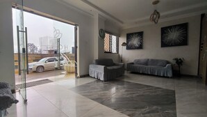 A spacious living room with a large glass door leading outside, a sofa, a chair, and two abstract wall art pieces. - Hoyjiifka Hotel Azora (Moyale)