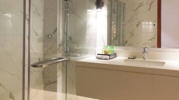Un baño moderno con ducha de vidrio, pared de azulejos de mármol, un espejo grande y una encimera con artículos de aseo.