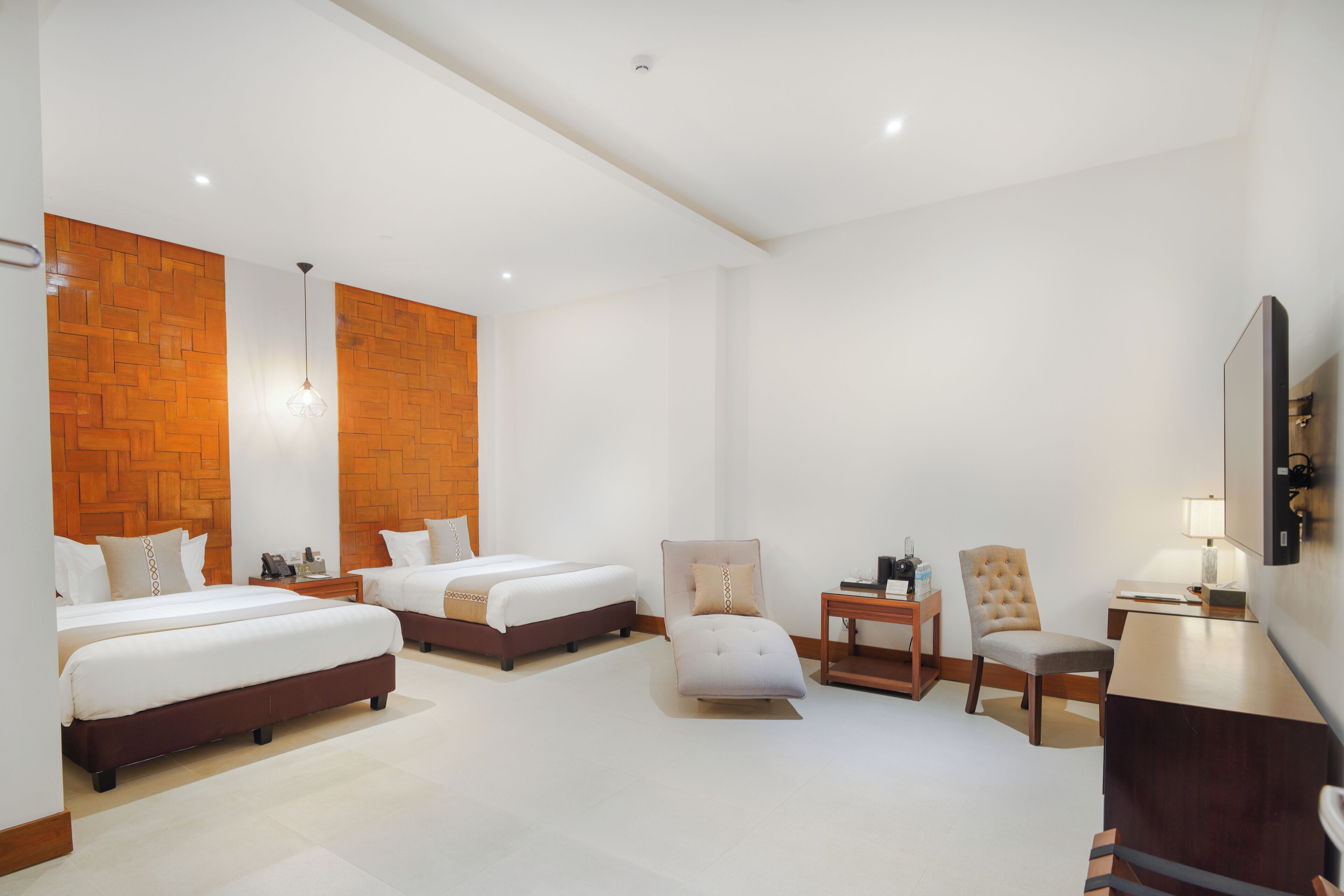 A hotel room with two beds, a desk, a chair, a lamp, and a TV.