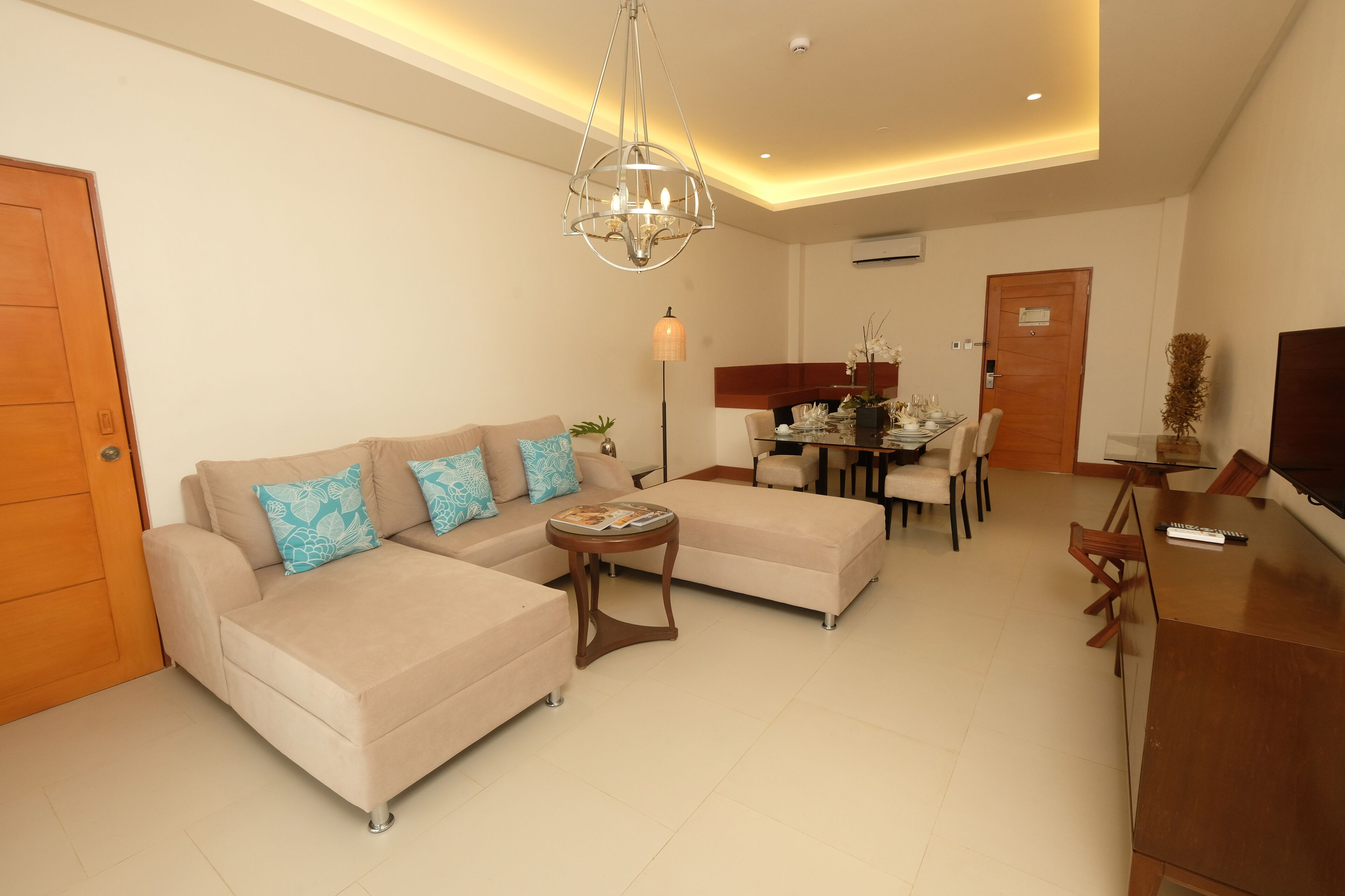A modern living room with a beige sofa, a coffee table, and a dining area with chairs and a table.