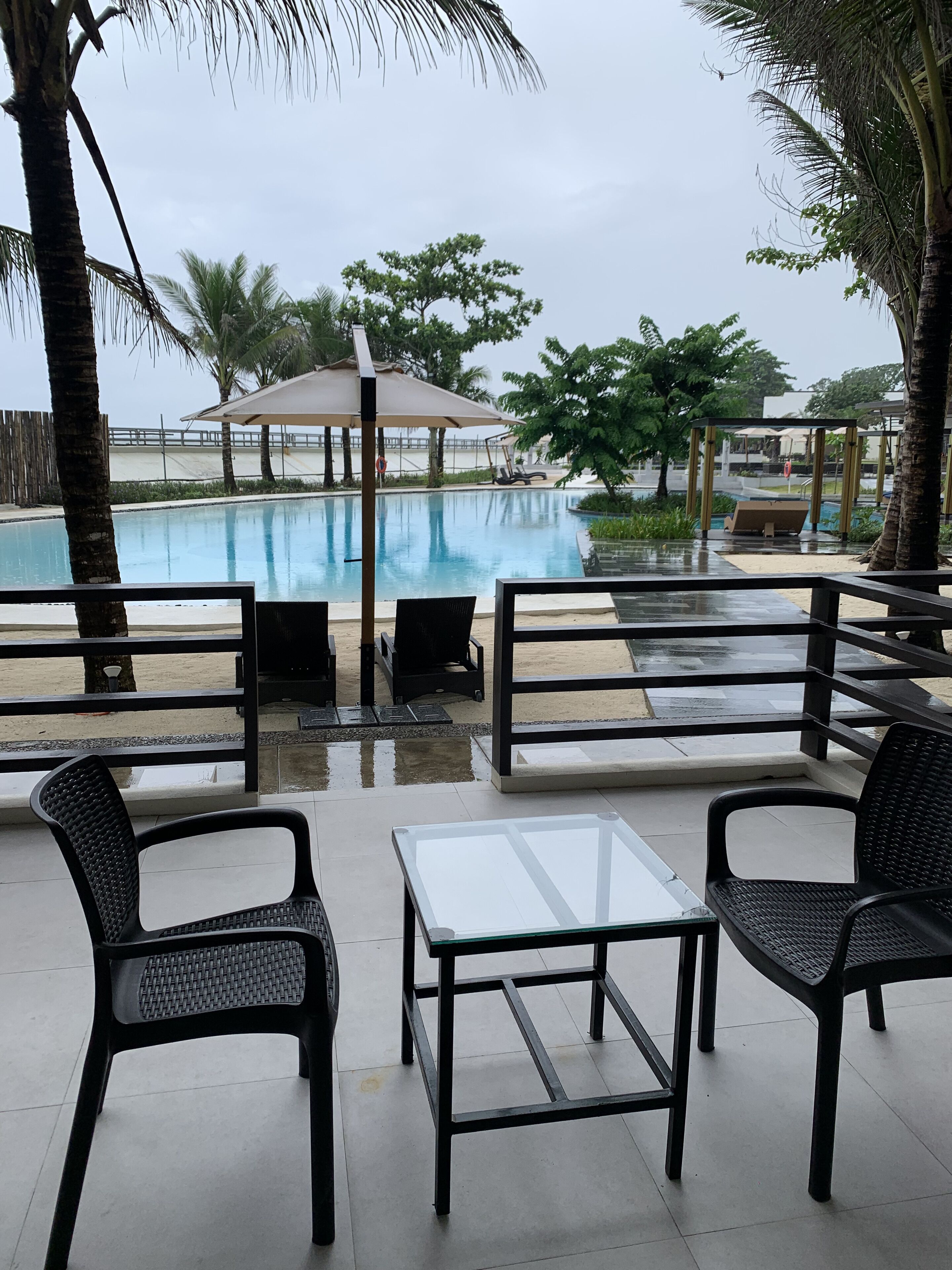 Ein Poolbereich mit Liegestühlen und einem Tisch, eine Palme und Blick auf den Pool.