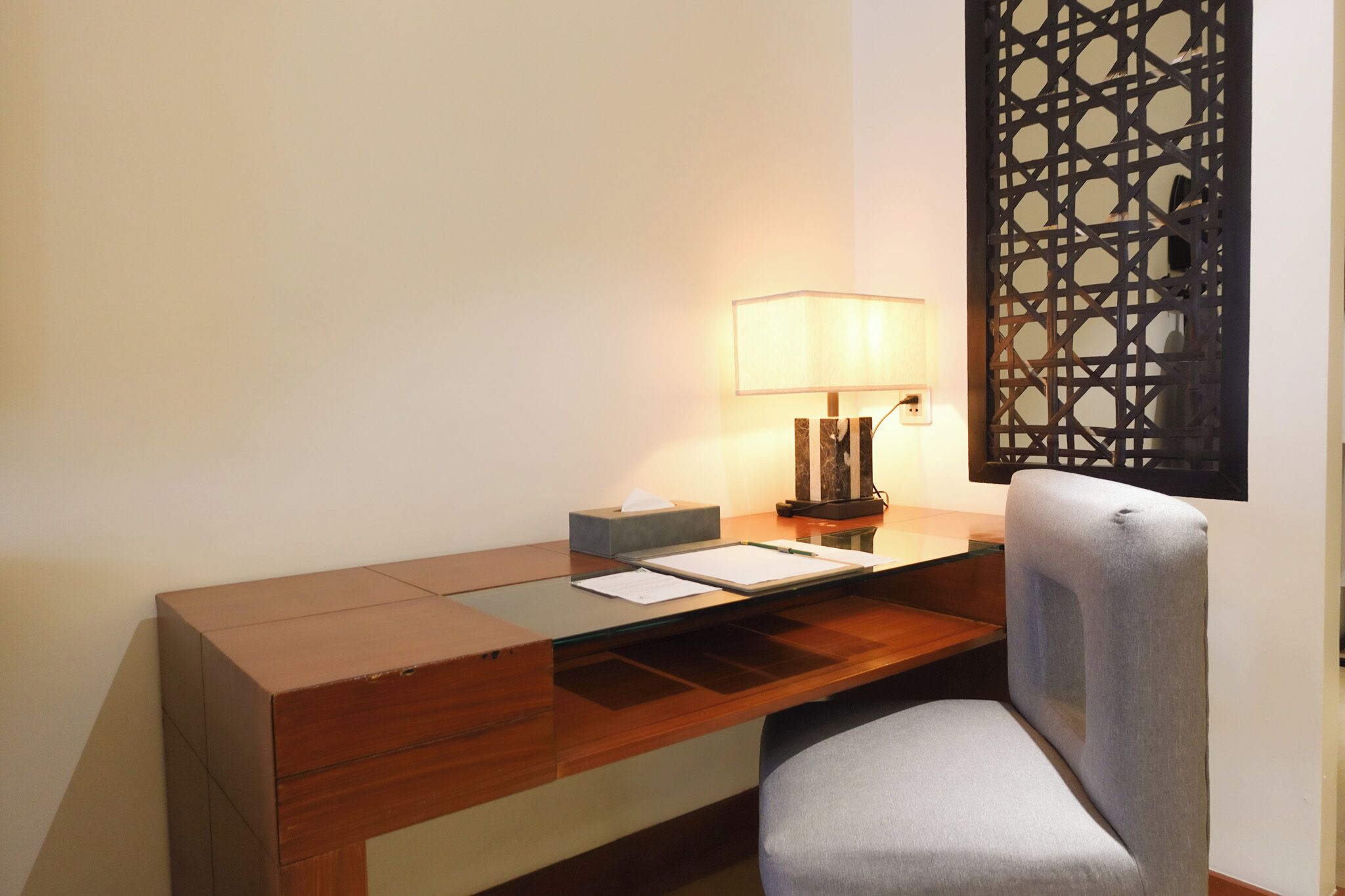A hotel desk with a lamp, a tissue box, and a chair.