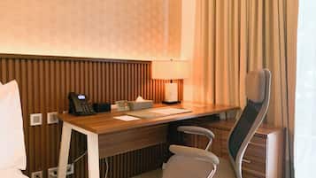 A hotel room with a wooden desk, a chair, a telephone, a lamp, and a bedside table.