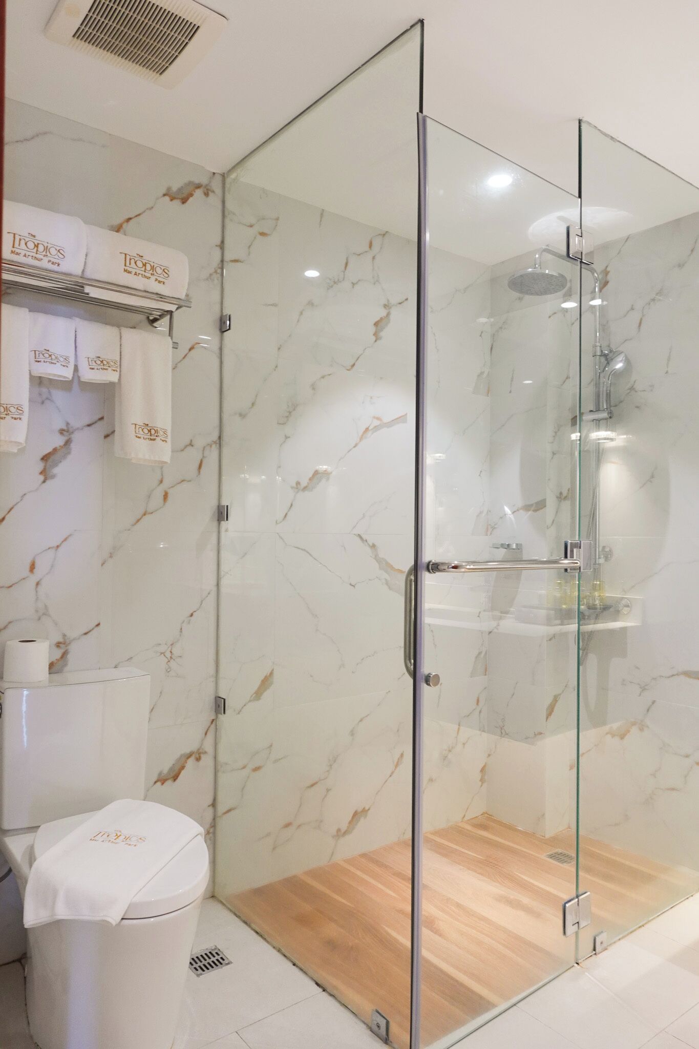 Un baño moderno con ducha de vidrio, paredes de mármol y suelo de madera.