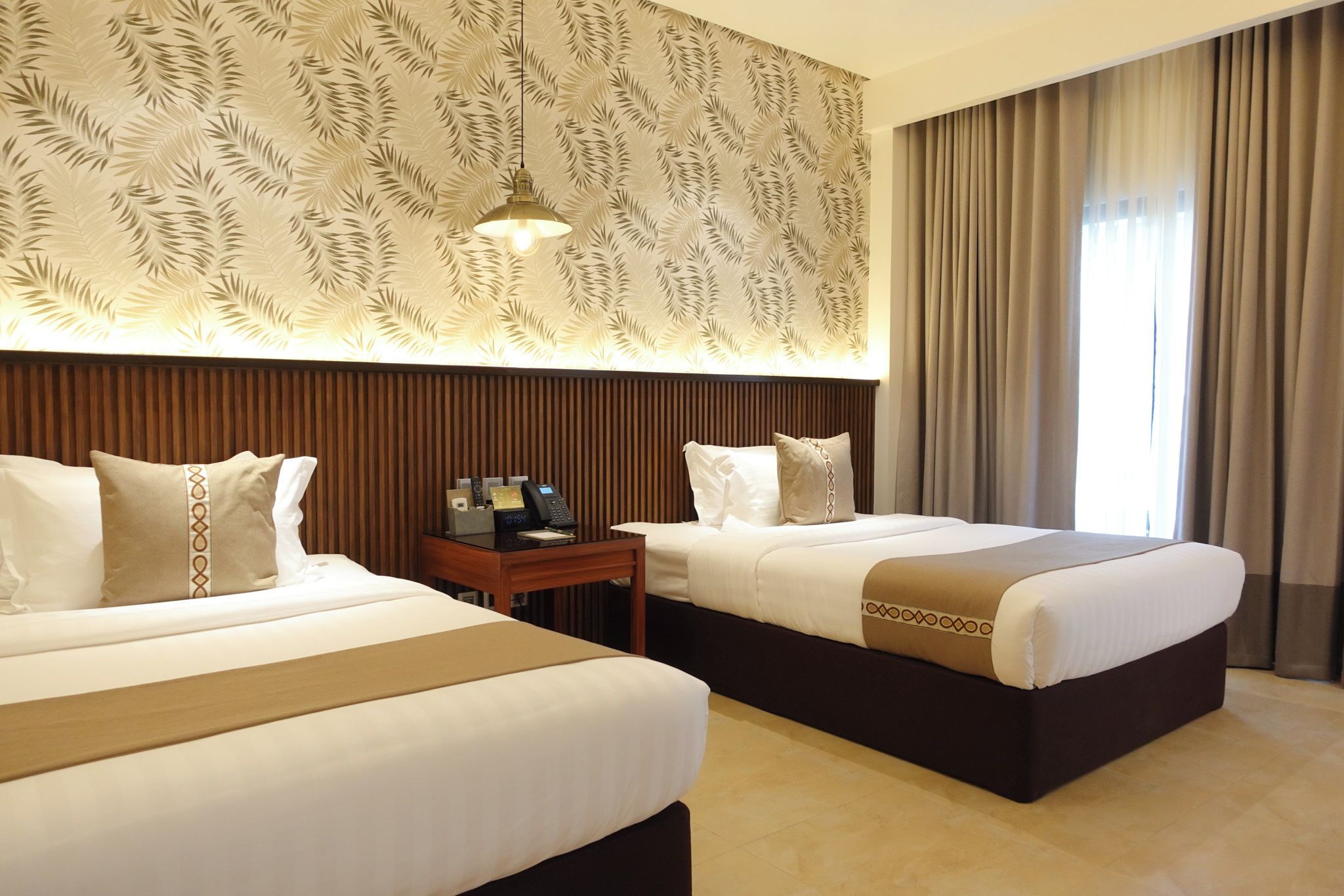 A hotel room with two beds, a wooden headboard, a nightstand with a phone, and a patterned wall.