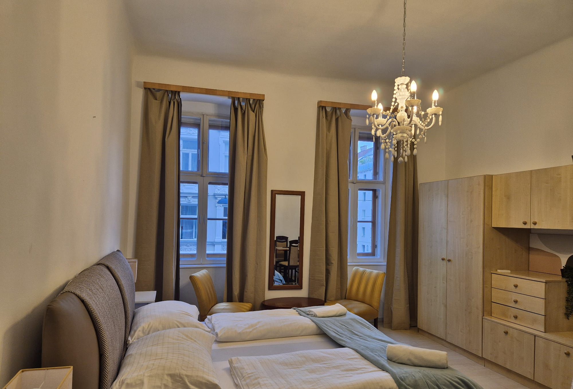 Une chambre à coucher comprenant un lit, deux chaises, un miroir, un lustre et une armoire.