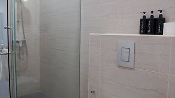 Un baño moderno con ducha de vidrio, inodoro blanco y estante con artículos de aseo.