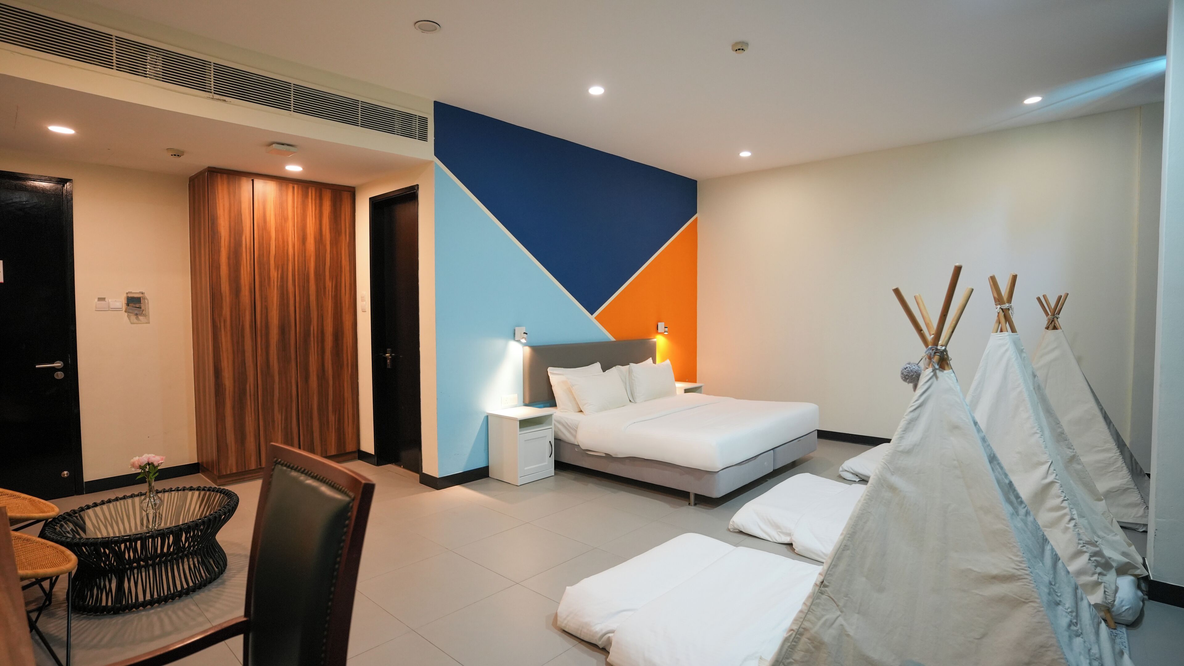 Una habitación de hotel moderna con una cama, mesitas de noche, una silla, una pequeña mesa con un florero y una decoración tipi.