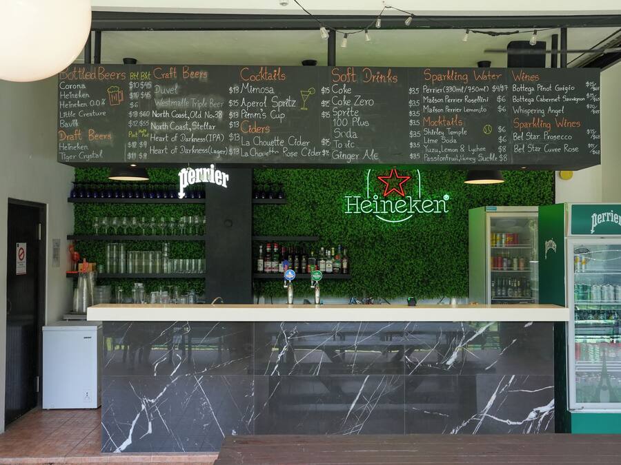 Zona de bar con una pizarra que muestra un menú de bebidas varias y un refrigerador de Perrier.