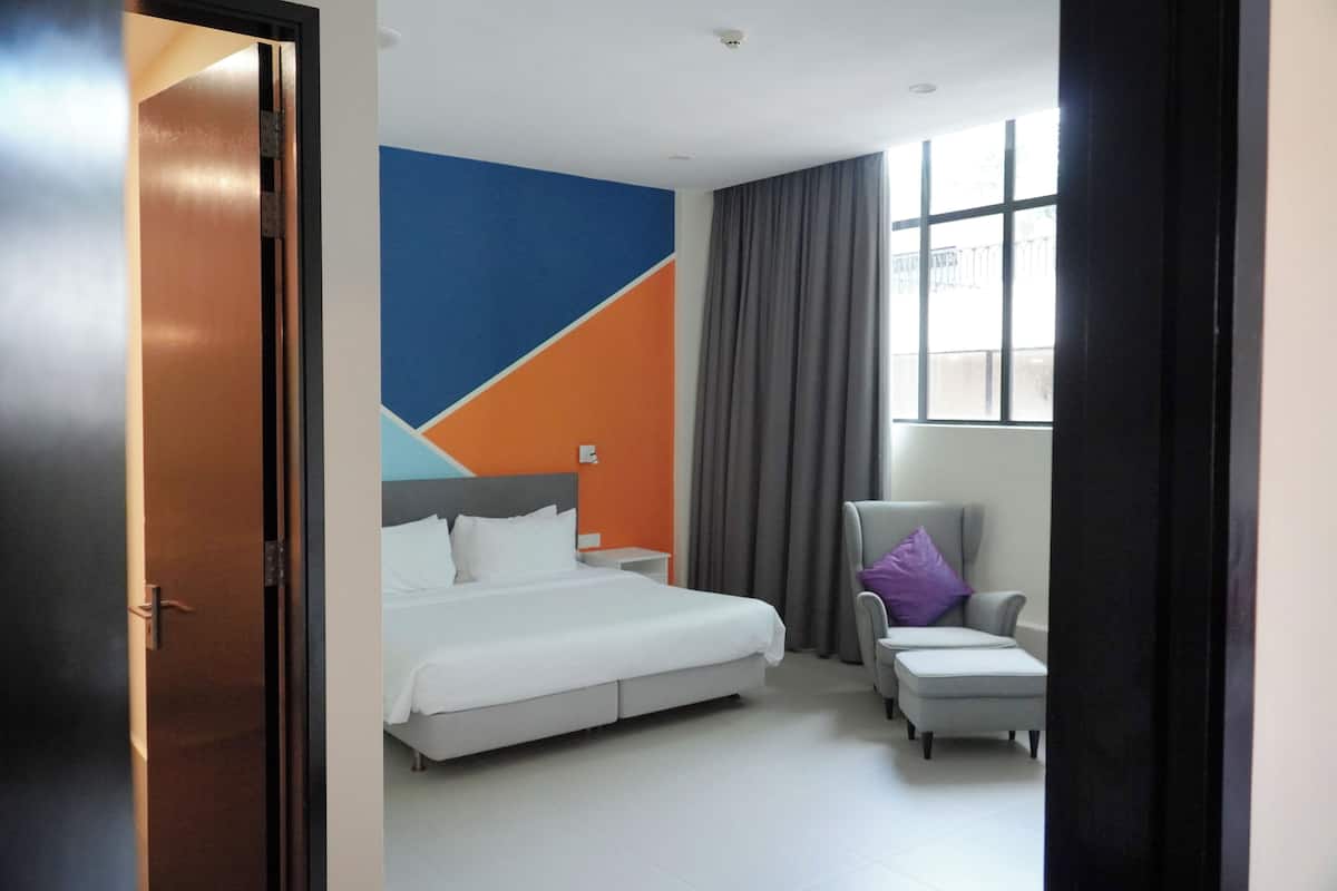 A hotel room with a bed, a chair, a window with curtains, and a wall with a geometric design.