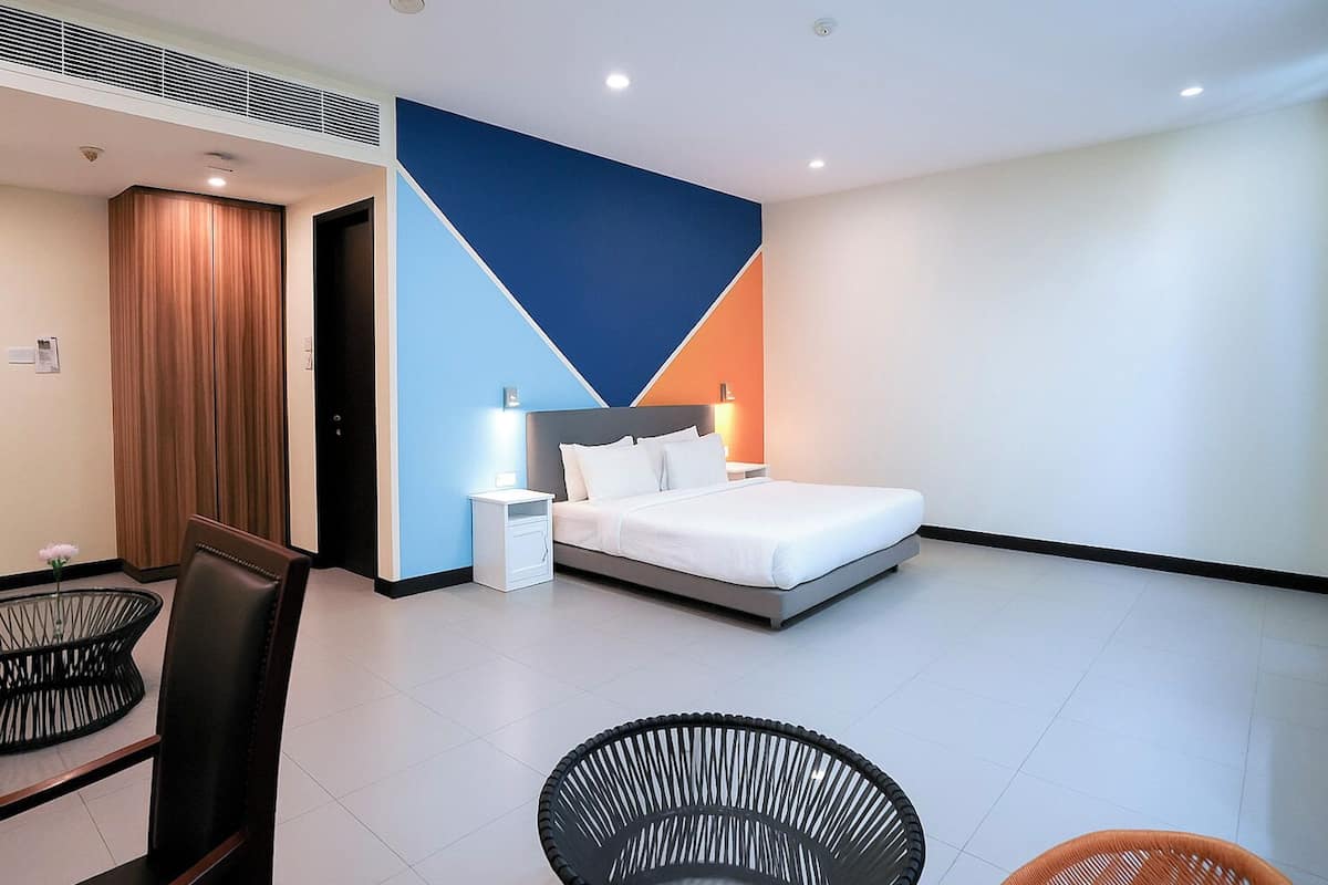 A modern hotel room with a bed, bedside tables, a chair, and a dining area with a table and chairs.