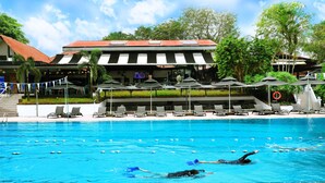 Piscina con dos personas nadando, rodeada de sillas de descanso y sombrillas.