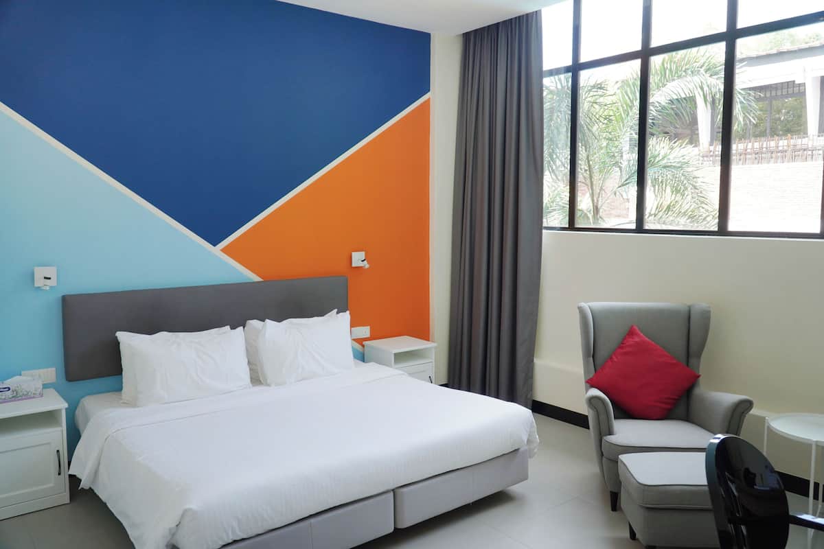 A hotel room with a bed, a chair, a small table, and a window with curtains.