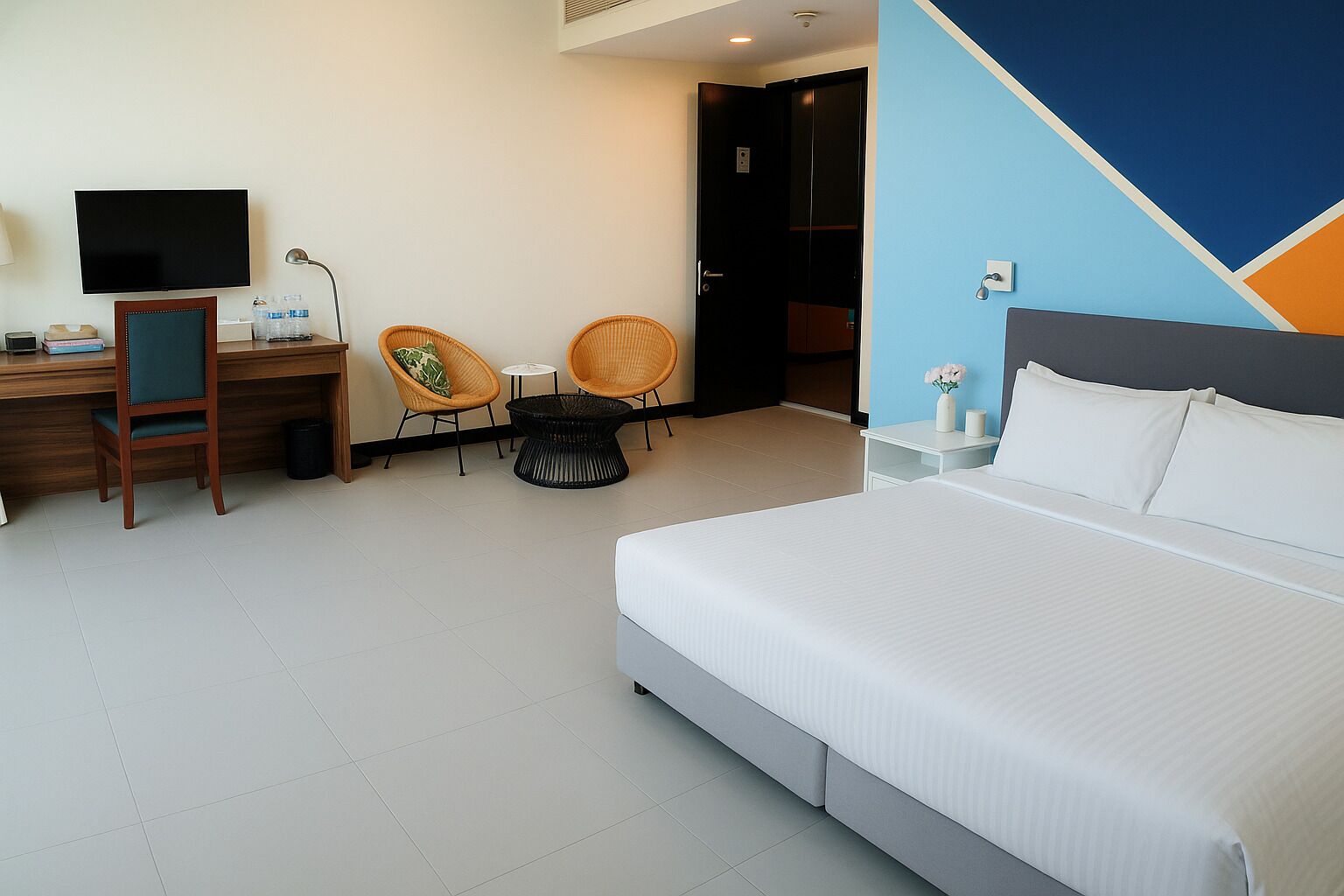 Habitación de hotel con cama, escritorio, computadora, dos sillas, una mesita y televisor.