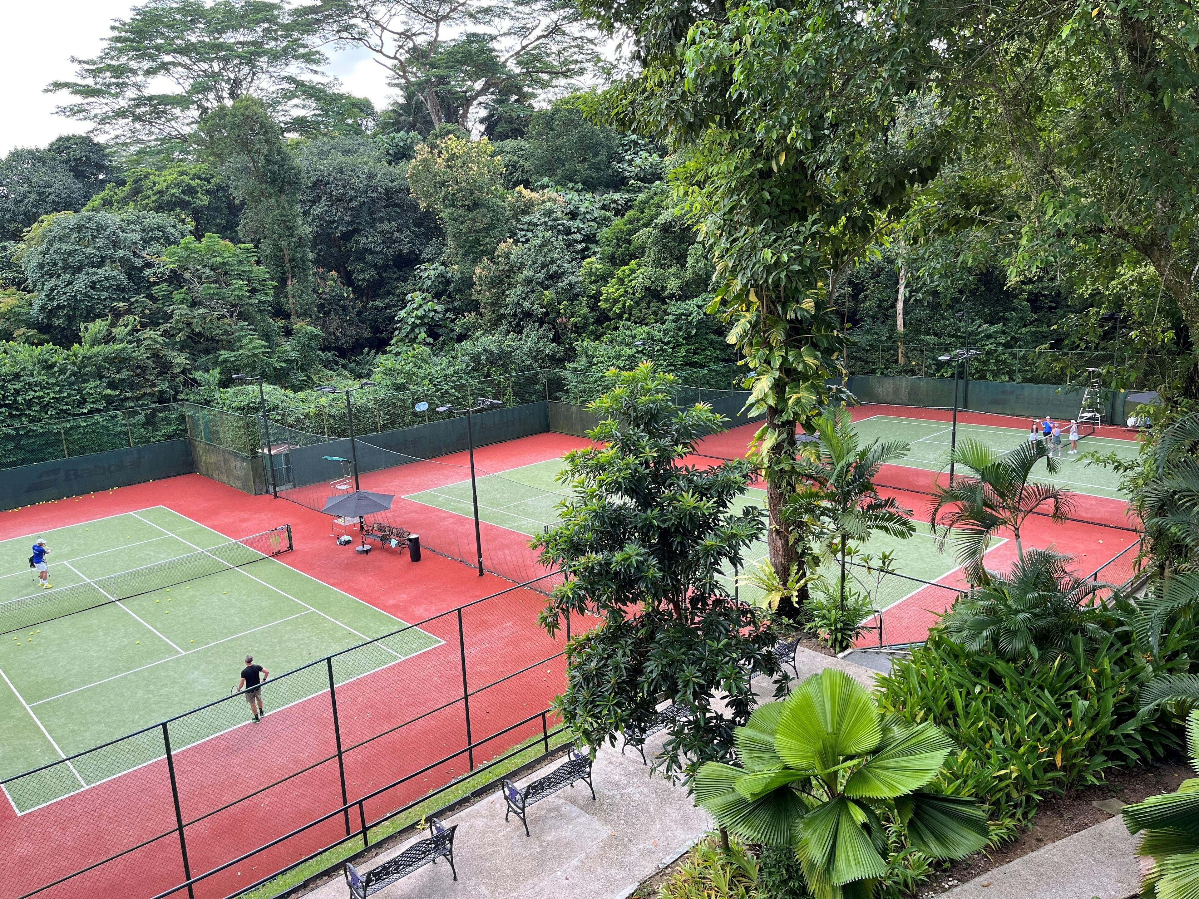 An outdoor tennis court surrounded by lush greenery.