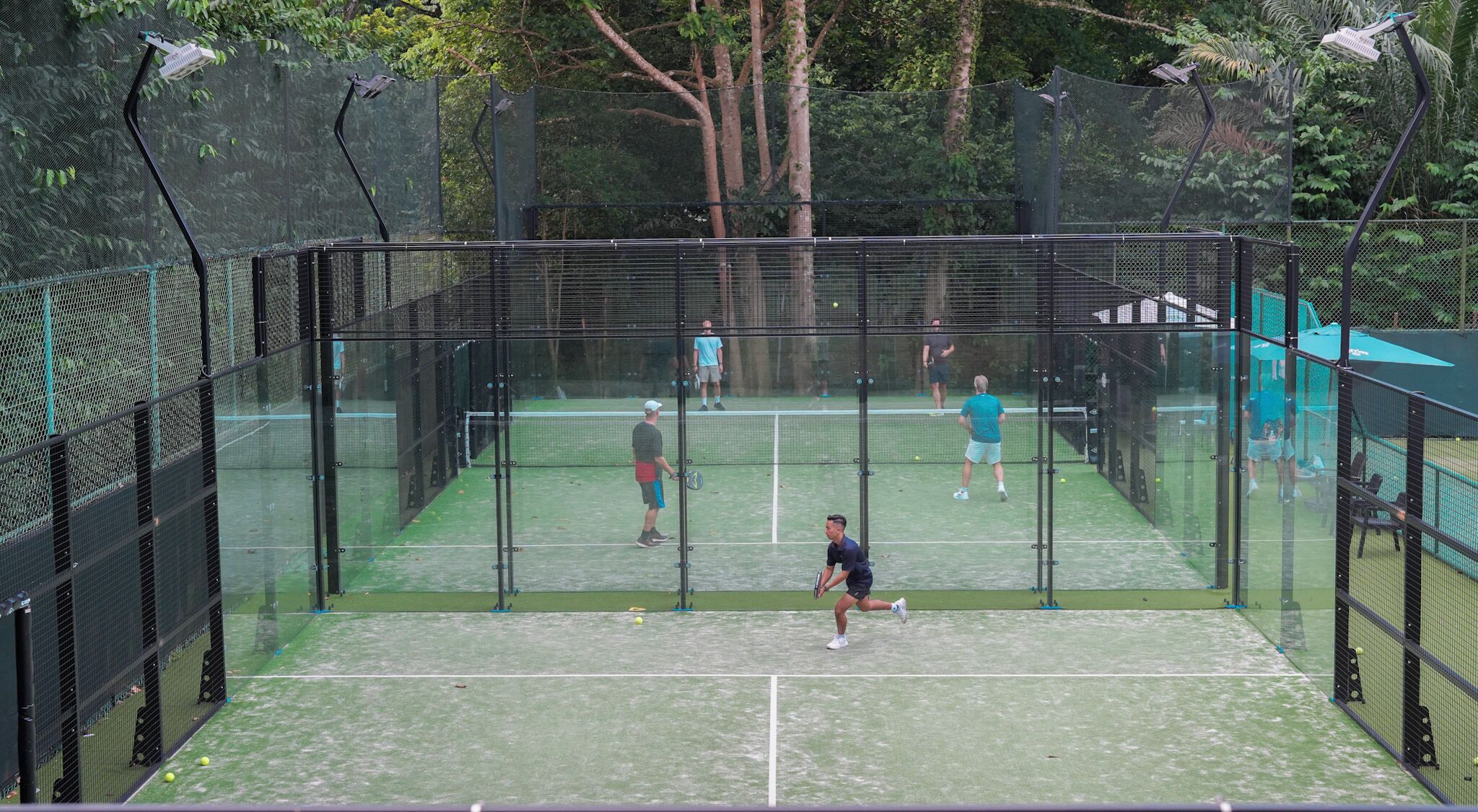 A tennis court enclosed by a netted fence with trees in the background.
