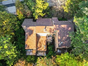 Eine Vogelperspektive eines Hauses, umgeben von dichter Vegetation, mit einem erkennbaren Dach und einer kleinen Terrasse.