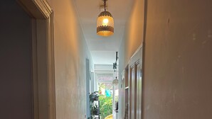 Een smalle gang met houten vloer, witte wanden en een plafondlamp.