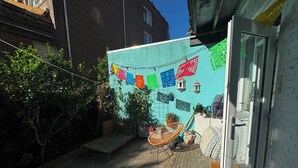 Een binnenplaats met een betegelde vloer, een houten bank en een deur naar een kamer met witte muren.