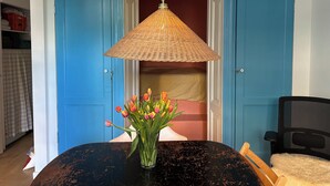 Een kamer met een blauwe deur, een zwarte tafel met een vaas tulpen en een rieten lamp.