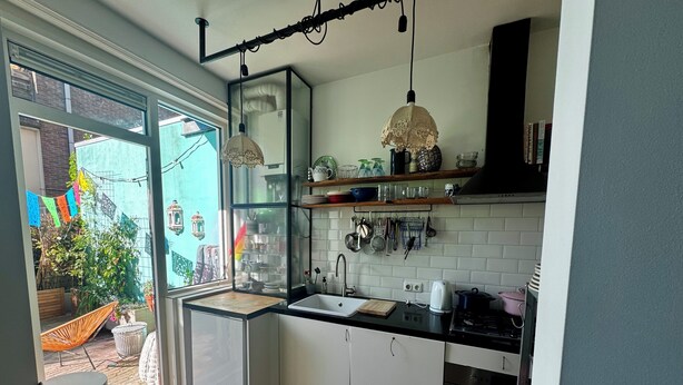 Een moderne keuken met een groot raam, witte kasten en een zwart aanrecht.