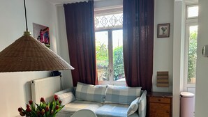Een gezellige kamer met een bank, een tafel met een vaas tulpen, een rieten lamp en een raam met gordijnen.
