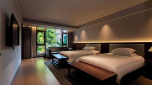 A modern hotel room with two beds, a flat-screen TV, a bench, and a large window offering a view of greenery. - Wu Yi Creekside Homestay (Jingdezhen)
