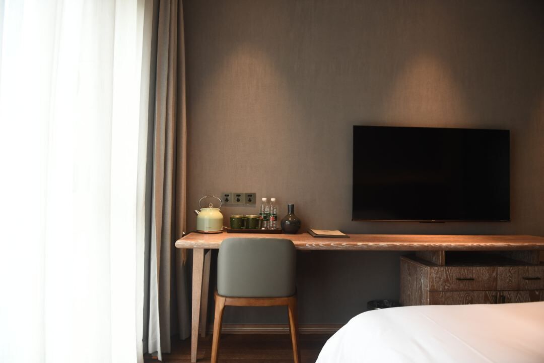 Habitación de hotel con cama, escritorio con silla, televisión de pantalla plana y una pequeña mesa con utensilios de cocina.