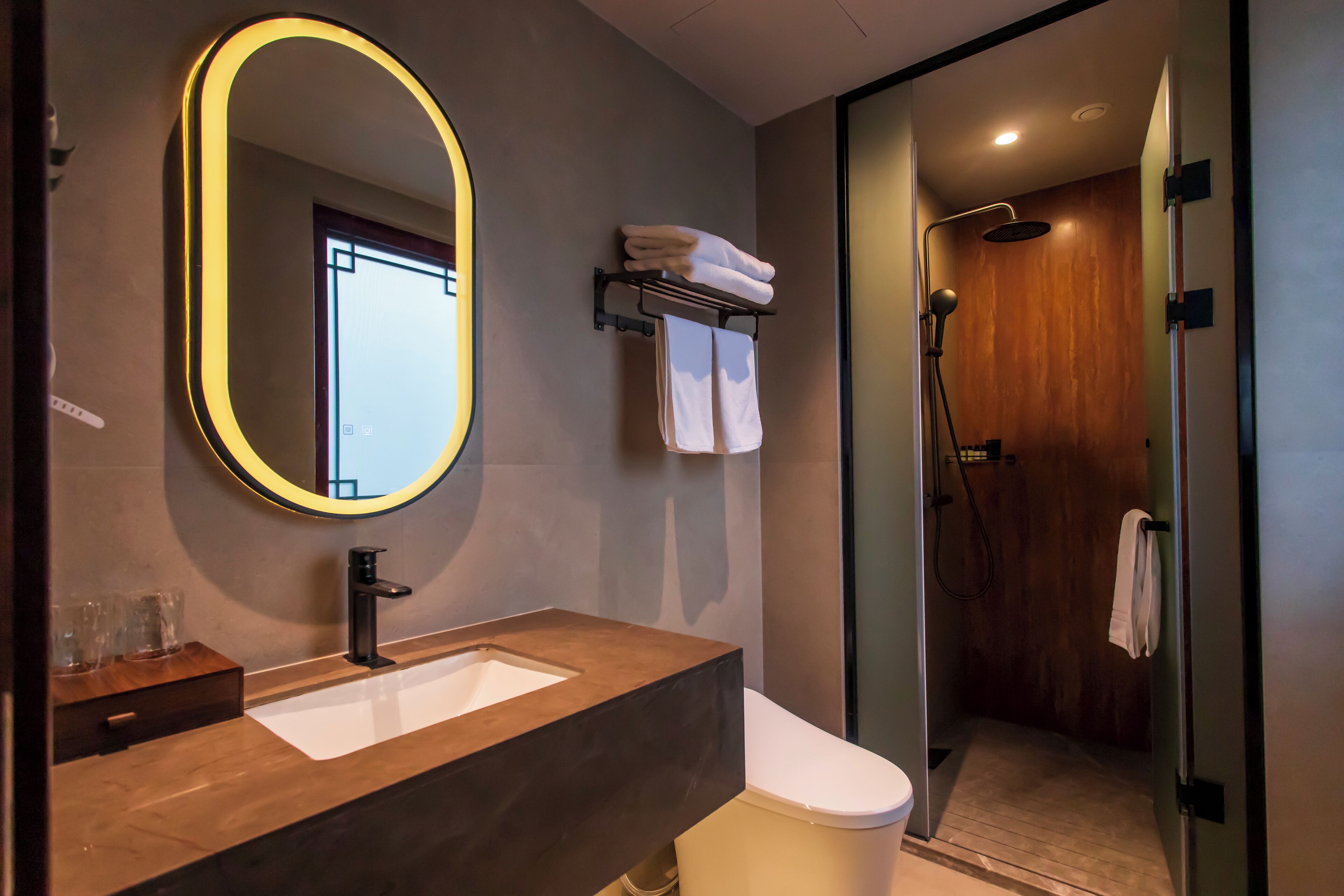 A modern bathroom with a large mirror, a wooden vanity, a white toilet, and a glass-enclosed shower area.