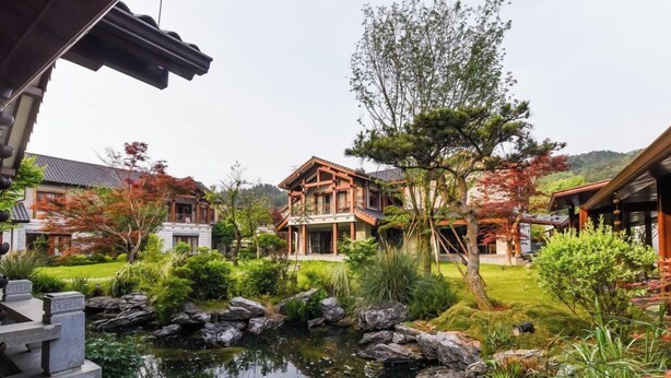 A traditional Japanese-style house with a koi pond, surrounded by lush greenery and a mountainous backdrop. - Wu Yi Creekside Homestay (Jingdezhen)