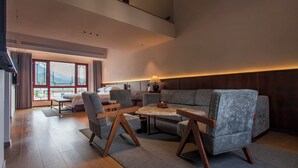 A modern living room with a sofa, chairs, a coffee table, and a desk. There is a large window with a view of mountains. - Wu Yi Creekside Homestay (Jingdezhen)