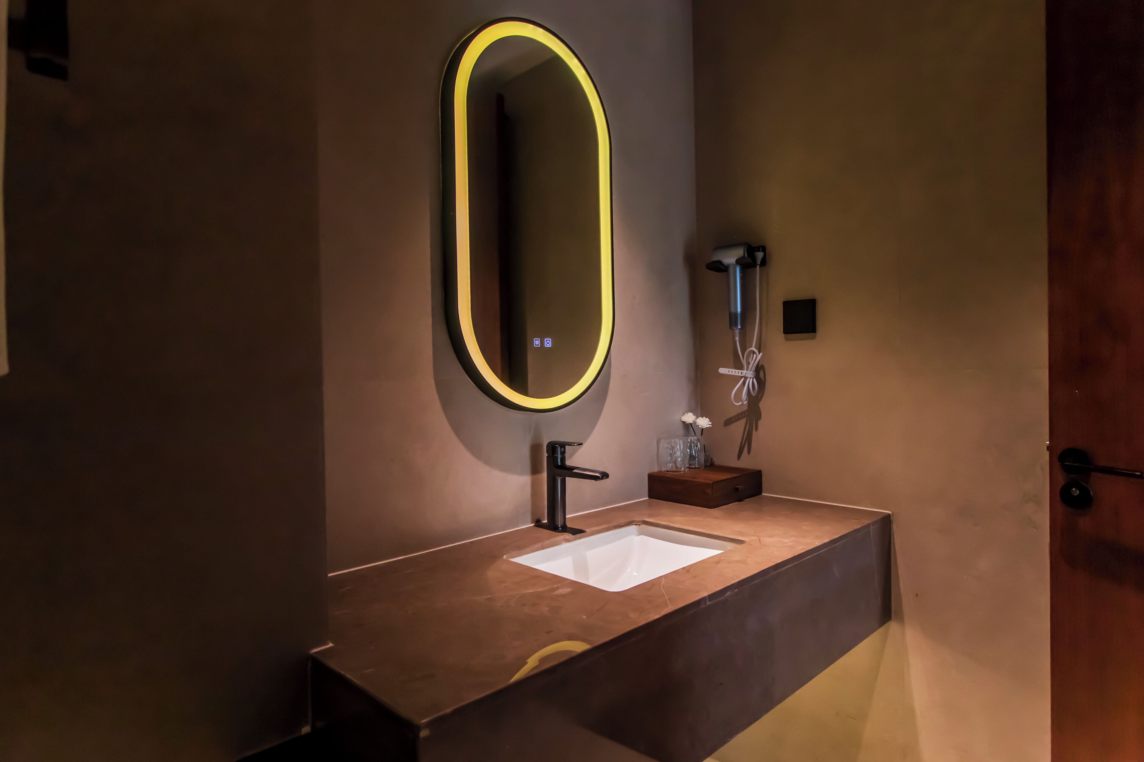A bathroom with a modern design, featuring a large mirror with a neon light, a sink, and a handheld showerhead.