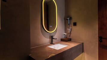 A bathroom with a modern design, featuring a large mirror with a neon light, a sink, and a handheld showerhead.