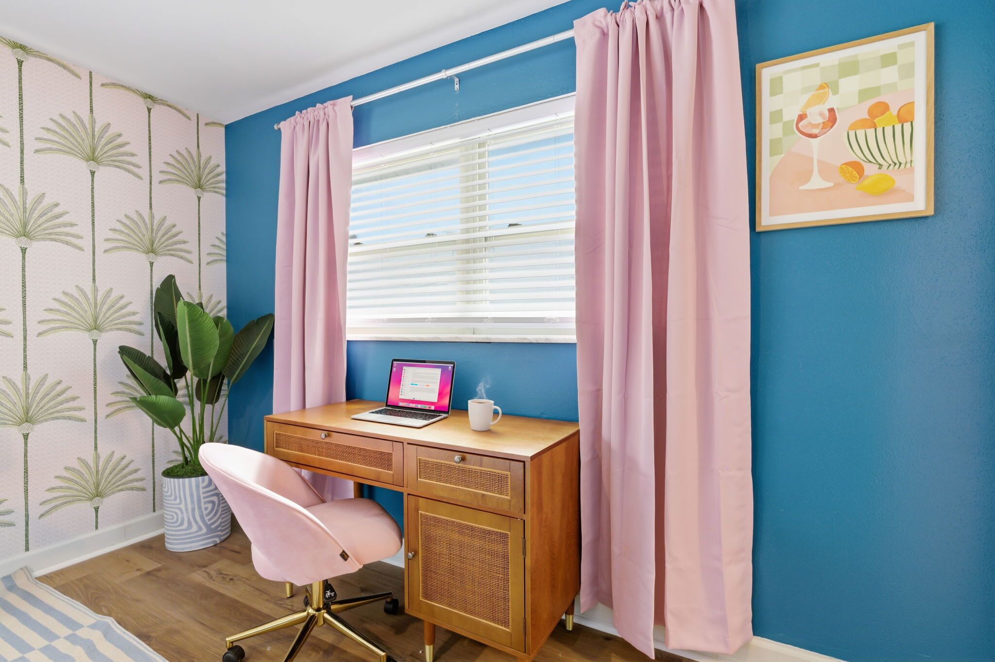 A room with a wooden desk, a pink chair, a laptop, a white mug, and a window with blinds.