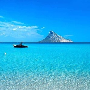 A clear blue sea with a boat and a distant mountain. - Villa Tavolara with Ocean View in Porto San Paolo (Porto San Paolo)