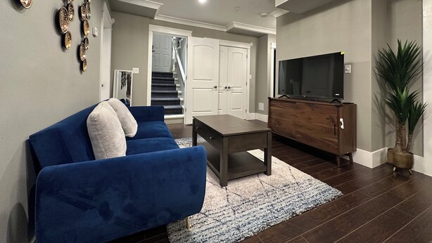 Una sala de estar con un sofá azul, un armario de madera, un televisor y una escalera que conduce a otra habitación.
