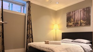 Un dormitorio con cama, mesita de noche, lámpara, un cuadro y una ventana con cortinas.