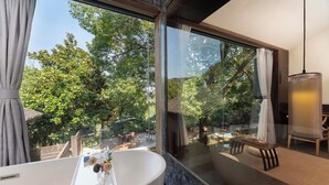 A modern bathroom with a large bathtub, a glass shower enclosure, and a view of a lush garden and outdoor seating area. - Lushimon Retrecrt (Hangzhou)