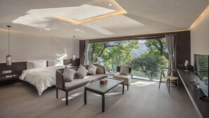 A modern hotel room with a large bed, a sofa, a coffee table, and a TV. The room has a large window with a view of trees and mountains. - Lushimon Retrecrt (Hangzhou)