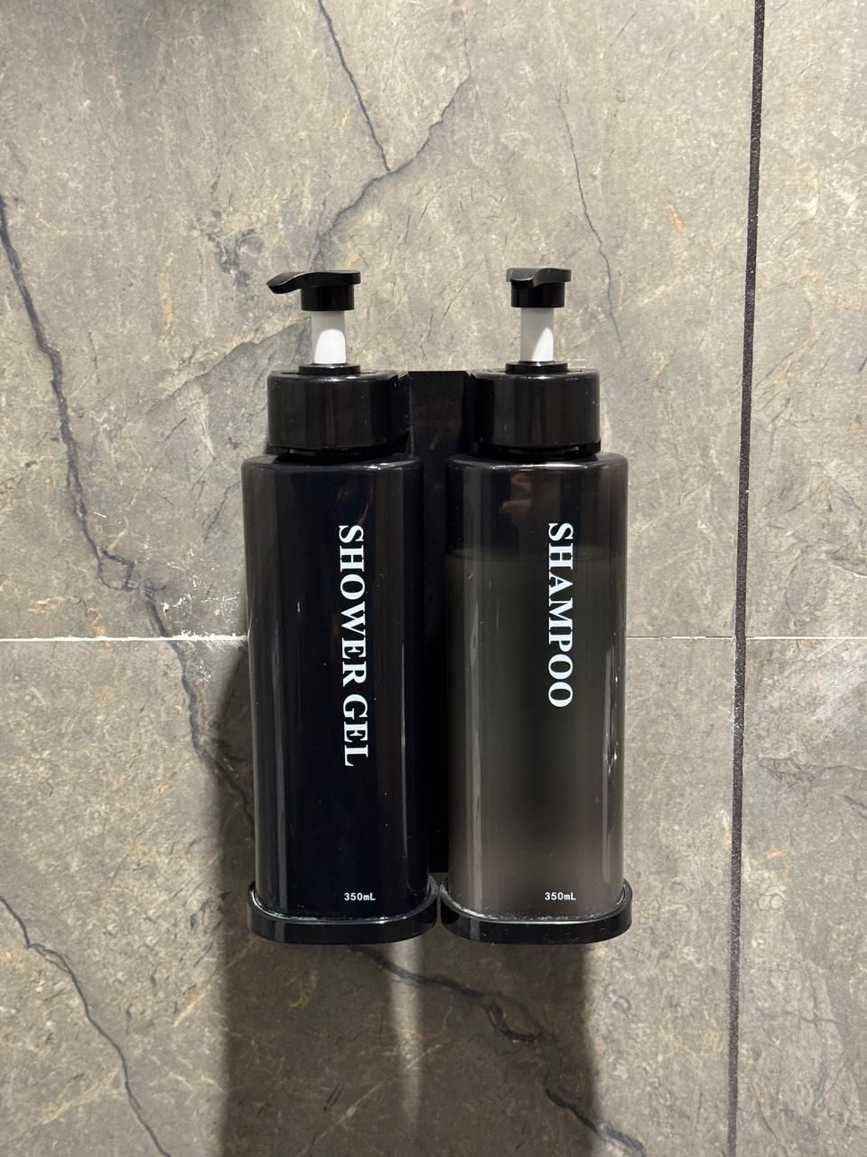 Two black bottles of shower gel and shampoo with pumps, each labeled with 350mL, against a textured stone wall.