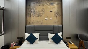Une chambre d’hôtel moderne avec un grand lit, un ventilateur de plafond, un tableau représentant un paysage et une table de chevet avec une télécommande.