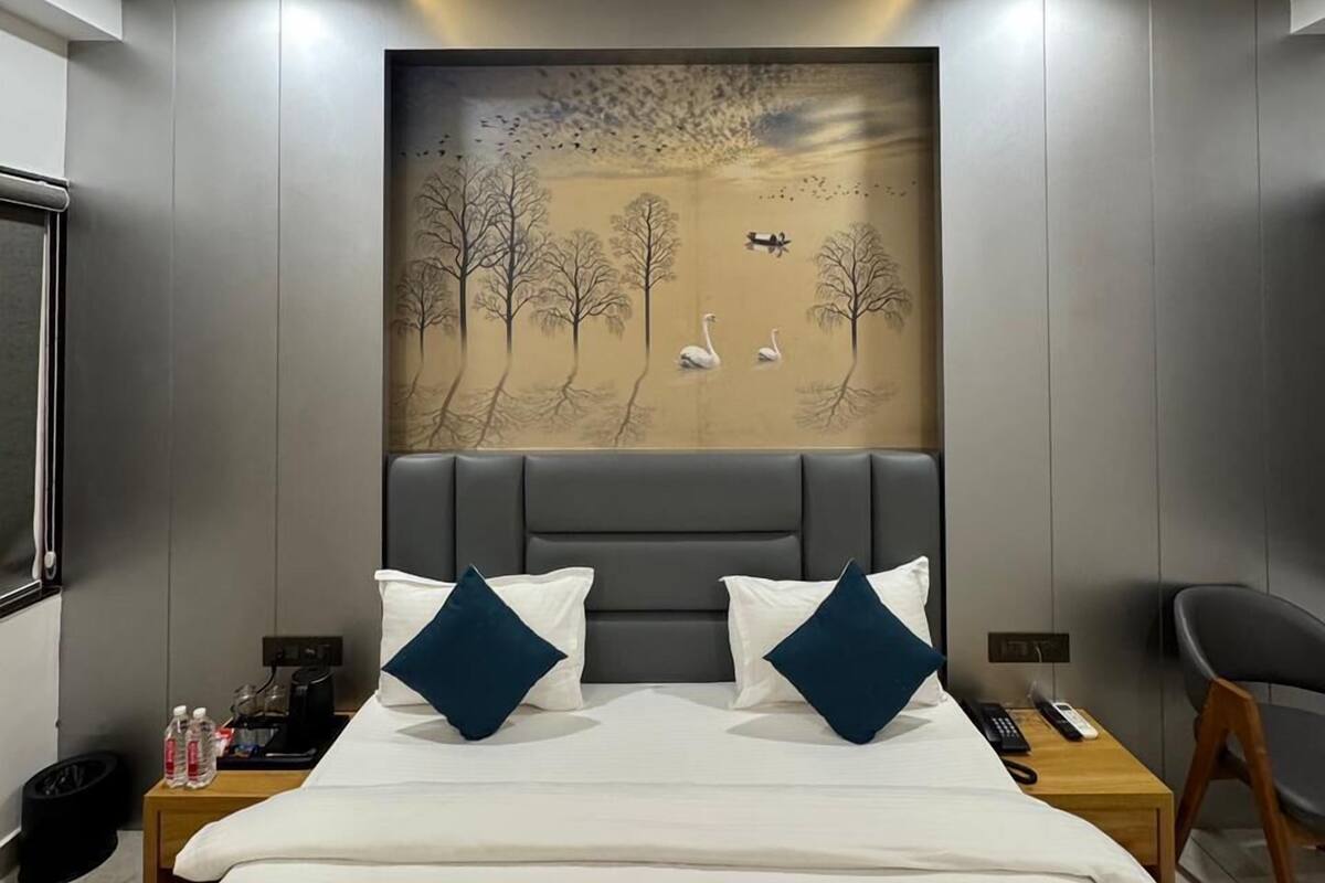A modern hotel room with a large bed, a ceiling fan, a painting of a landscape, and a nightstand with a remote control.