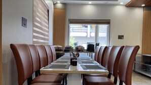 Une salle de conférence avec une longue table, des fauteuils en cuir marron, un ventilateur de plafond et une fenêtre avec des stores.