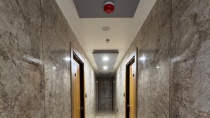 Un couloir aux murs et aux portes en marbre, qui mène à un ascenseur.