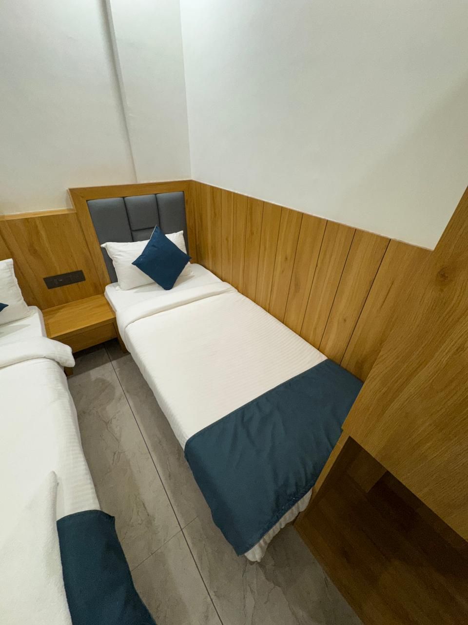 A hotel room with two single beds, wooden headboards, and a tiled floor.
