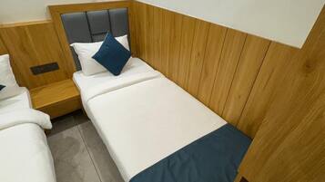A hotel room with two single beds, wooden headboards, and a tiled floor.